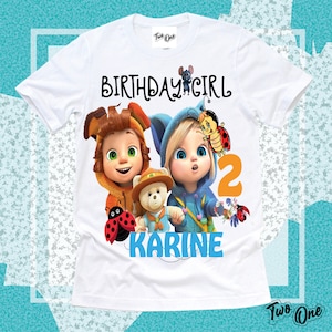 Könnte beinhalten: Weißes T-Shirt mit einem Geburtstags-Mädchen-Design mit zwei Comicfiguren, einem Teddybär und Marienkäfern. Der Text "Birthday Girl" und die Zahl "2" sind auf dem Shirt gedruckt. Der Name "Karine" ist in Blau unter den Figuren gedruckt.