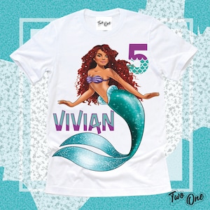 May include: White t-shirt with a mermaid illustration. The mermaid has long red hair, a purple seashell bra, and a teal tail. The text "VIVIAN" is printed in purple below the mermaid. The number "5" is printed in purple with teal scales on the right side of the image.