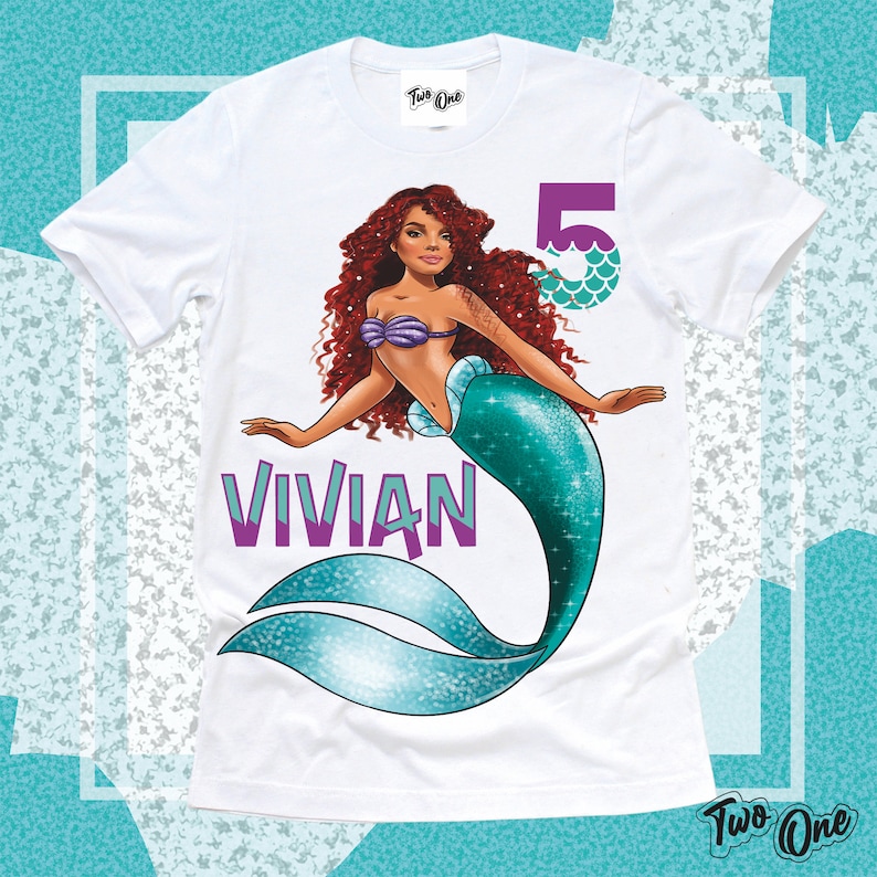 May include: White t-shirt with a mermaid illustration. The mermaid has long red hair, a purple seashell bra, and a teal tail. The text "VIVIAN" is printed in purple below the mermaid. The number "5" is printed in purple with teal scales on the right side of the image.