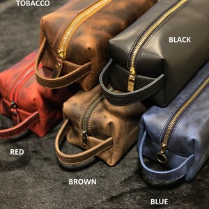 May include: Five leather zippered pouches in different colors: red, brown, tobacco, black, and blue. Each pouch has a gold zipper and a leather handle.
