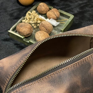 May include: A brown leather zippered pouch with a distressed finish. The pouch is open and the inside is visible.