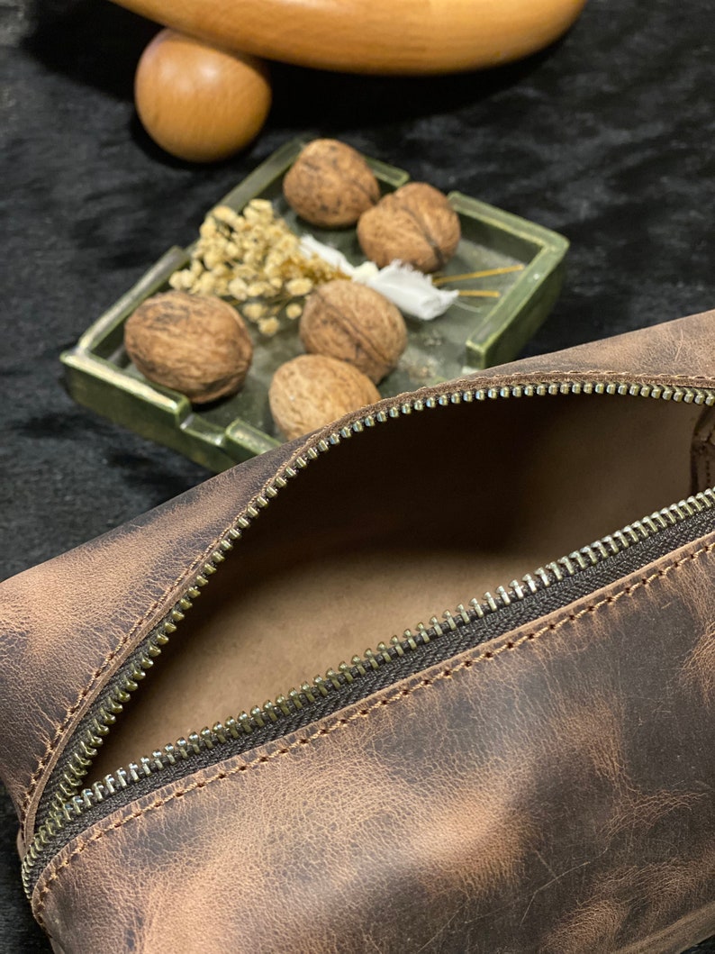 May include: A brown leather zippered pouch with a distressed finish. The pouch is open and the inside is visible.