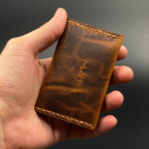 May include: A brown leather wallet with a distressed finish and stitching around the edges.