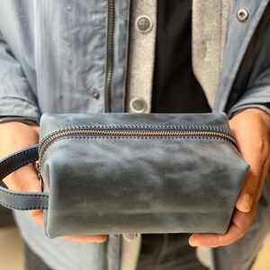 May include: A dark blue leather travel toiletry bag with a zipper closure and a leather handle.