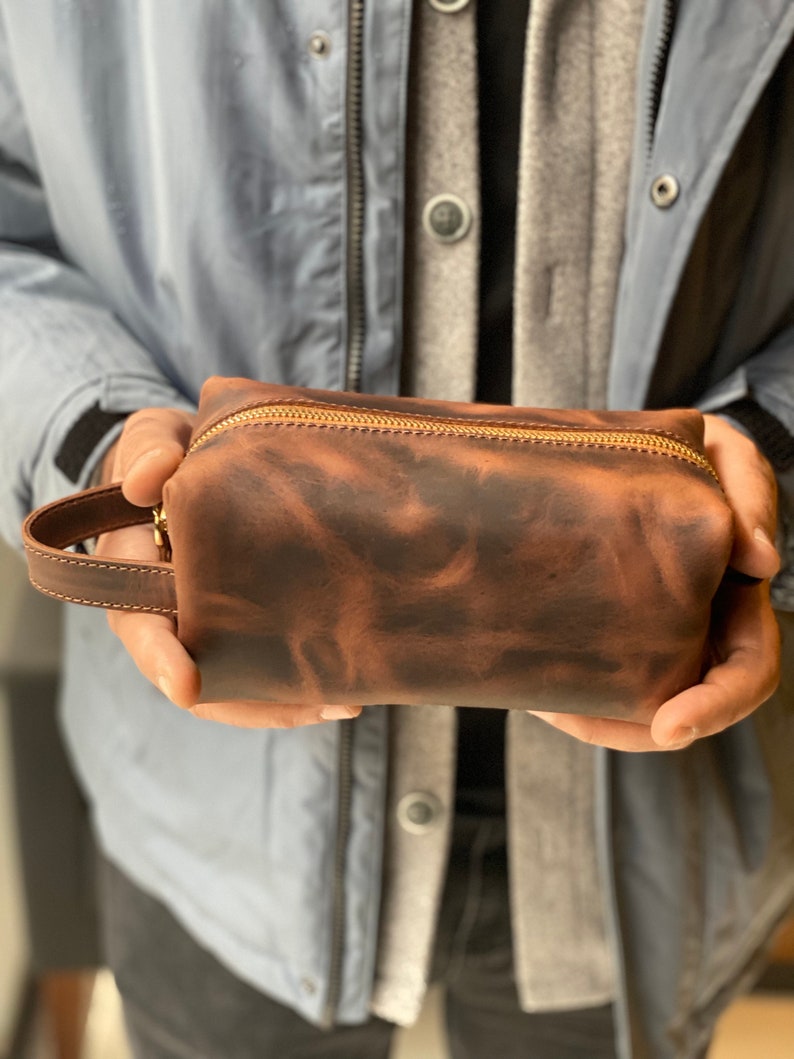 May include: A brown leather zippered pouch with a gold zipper. The pouch has a textured, distressed look.