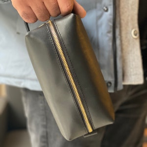May include: A black leather zippered toiletry bag with a gold zipper.