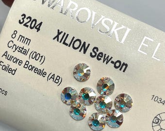 May include: A close-up of several iridescent Swarovski XILION sew-on crystals, each 8 mm in diameter. The crystals are labeled "Aurore Boreale (AB)" and are displayed on a white card with the Swarovski logo and product details.