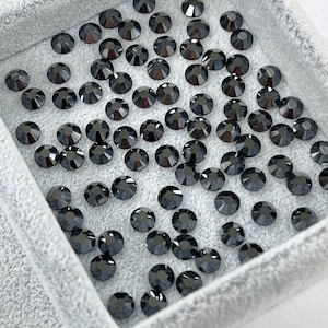 May include: A collection of small, round, black rhinestones with multiple facets, displayed in a light gray velvet tray. The rhinestones are evenly distributed, reflecting light and creating a sparkling effect. Ideal for crafting and embellishment.