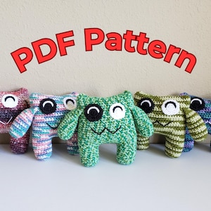 Op de afbeelding: Een rij kleurrijke, gehaakte monstertjes met grote ogen en lachende monden. De speeltjes zijn in roze, blauw, groen en paars. De tekst "PDF Pattern" staat in het rood, in een boog erboven.
