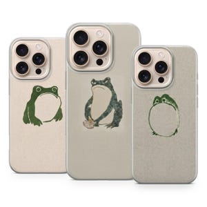 Pode incluir: Três capas transparentes para smartphone com ilustrações de sapos verdes. A capa da esquerda mostra um sapo sentado, a central um sapo a comer de uma taça e a da direita um design circular de sapo. Cada capa tem uma abertura para a câmara.