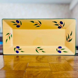 Può includere: Un piatto da portata rettangolare in ceramica gialla con un bordo verde e disegni di rami di ulivo dipinti in verde, rosso e blu.