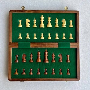 Op de afbeelding: Een houten schaakset met een groene vilt binnenkant. De schaakstukken zijn tweekleurig, met lichte en donkere houten stukken. De set is open en toont alle stukken in hun aangewezen sleuven.