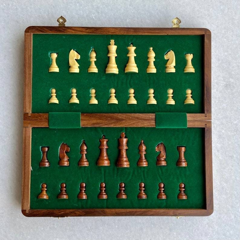 Op de afbeelding: Een houten schaakset met een groene vilt binnenkant. De schaakstukken zijn tweekleurig, met lichte en donkere houten stukken. De set is open en toont alle stukken in hun aangewezen sleuven.