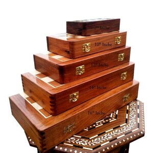 Op de afbeelding: Een stapel houten schaak- en speldozen in verschillende maten, vari&euml;rend van 18 cm tot 41 cm. De dozen zijn diep bruin van kleur met goudkleurige sluitingen. De schaakborden hebben een licht en donker vierkant patroon.