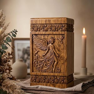 Può includere: Un'urna di legno con un angelo scolpito. L'urna rettangolare presenta un rilievo dettagliato di un angelo con le ali spiegate, circondato da colibrì. La parte superiore e inferiore sono decorate con rose scolpite. Una candela brucia sullo sfondo.