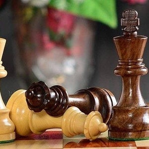 Op de afbeelding: Schaakspel met houten stukken op een schaakbord. Twee ivoorkleurige koningen staan rechtop, terwijl een donkerbruine koning en een gevallen ivoorkleurige koning op het bord liggen. De stukken zijn fijn gesneden, wat de strategie van het spel laat zien.