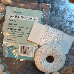 Puede incluir: Un difusor de ducha de roca volcánica blanca con forma de rosquilla, una cuerda de poliéster blanca y un paquete con el texto "Lava Rock Shower Diffuser". El peso neto es de 25g. El producto está diseñado para ser utilizado con aceites esenciales.