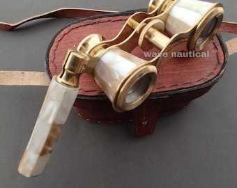May include: Antique brass opera glasses with mother-of-pearl accents. The binoculars are resting on a brown leather case with a strap. The text "wave nautical" is visible on the case.