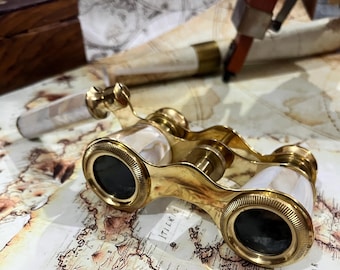 May include: Gold-tone opera glasses with mother-of-pearl accents. The glasses are closed and have a decorative design.