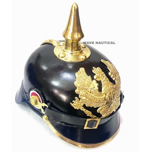 May include: A black Prussian Pickelhaube helmet with a gold-colored spike and decorative eagle emblem. The helmet features a leather chin strap and gold-colored trim. The text "WAVE NAUTICAL" is visible.