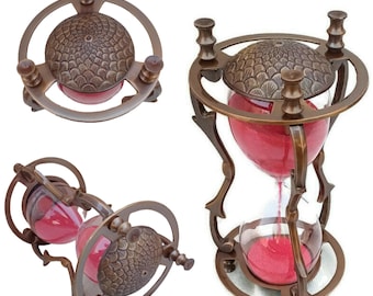 Op de afbeelding: Een antieke zandloper met een bronzen metalen frame. De zandloper bevat rood zand en heeft een decoratieve, getextureerde boven- en onderkant. Het ontwerp heeft een cirkelvormig frame en sierlijke details.