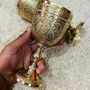 以下が含まれることがあります： 複雑なデザインが施された、金色の金属製のゴブレットが2つ。ゴブレットは丸いボウルと、広がったベースを持つステムを持っています。