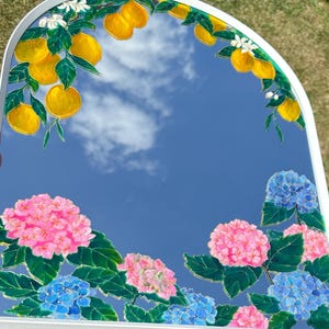 Puede incluir: Un espejo de pared arqueado con dise&ntilde;os bot&aacute;nicos pintados a mano. El borde superior muestra limones amarillos con hojas verdes y flores blancas. La secci&oacute;n inferior est&aacute; decorada con racimos de flores de hortensia rosas y azules.
