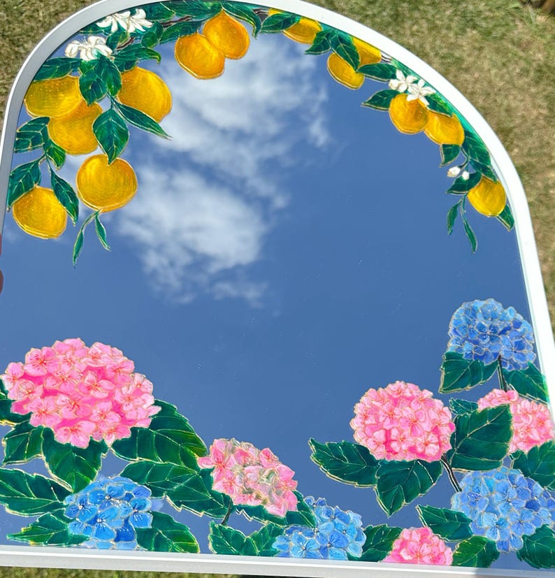 Puede incluir: Un espejo de pared arqueado con dise&ntilde;os bot&aacute;nicos pintados a mano. El borde superior muestra limones amarillos con hojas verdes y flores blancas. La secci&oacute;n inferior est&aacute; decorada con racimos de flores de hortensia rosas y azules.