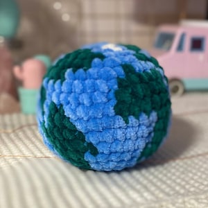 Può includere: Un globo terrestre fatto a mano in morbido tessuto, nei toni del blu e del verde. La superficie strutturata della sfera rappresenta i continenti e gli oceani. Il giocattolo è progettato per assomigliare a una versione in miniatura del pianeta.