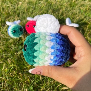 Può includere: Un set di peluche di api all'uncinetto in vari colori, tra cui verde, blu, bianco e rosso. I peluche hanno occhi neri e piccole ali.
