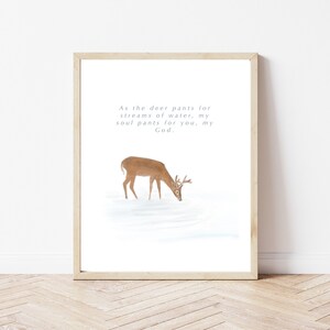 Könnte beinhalten: Ein gerahmter Druck mit einer Aquarell-Illustration eines Hirsches, der aus einem Bach trinkt. Der Druck zeigt das Zitat "Wie der Hirsch nach Wasser lechzt, so sehnt sich meine Seele nach dir, mein Gott."