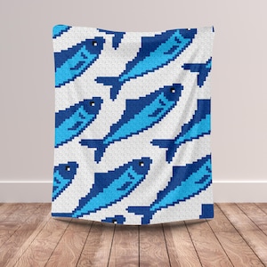 May include: A white blanket with a repeating pattern of pixelated blue fish. The fish are in various shades of blue, with dark blue outlines and details. The blanket is draped over a surface, showcasing the design.