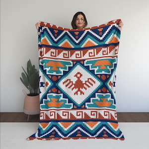 May include: A colorful blanket with a geometric pattern in shades of blue, orange, teal, and white. The design features a central diamond with a bird-like figure, surrounded by repeating geometric shapes. The blanket is held up, showcasing its full design.