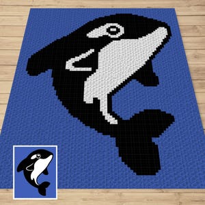 May include: A blue blanket featuring a large, pixelated orca whale design in black and white. The orca is positioned diagonally across the blanket. A smaller image of the orca is in the lower left corner. The blanket is on a wooden surface.