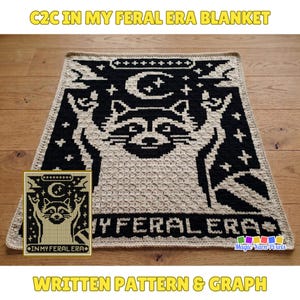 Può includere: Una coperta rettangolare all'uncinetto con un design pixelato nero e crema raffigurante un procione con le zampe alzate, una luna crescente e stelle. Il testo "IN MY FERAL ERA" è visualizzato in basso. Il bordo è color crema.