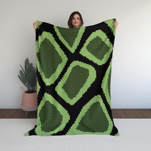 May include: A large blanket with a repeating geometric pattern. The design features lime green shapes outlined in a lighter green against a black background. The blanket is made of a soft material.