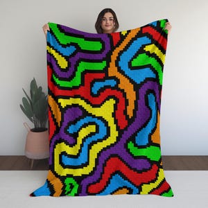 May include: A colorful blanket with a pixelated design. The blanket features a vibrant pattern of swirling lines in red, orange, yellow, green, blue, and purple, set against a black background. The blanket is held up by a person.