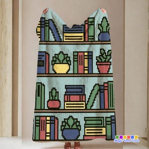 Può includere: Una coperta azzurra con un motivo in pixel art di scaffali pieni di libri colorati e piante in vaso. Il design presenta ripiani marroni orizzontali e varie forme rettangolari di libri nelle tonalità del rosso, verde, blu e giallo.