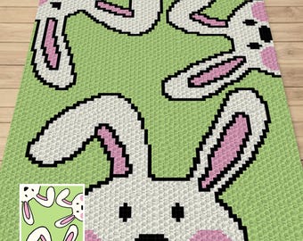 May include: A green crochet blanket with a white bunny rabbit design. The bunny has pink ears and a black nose. The bunny is peeking out from behind the edge of the blanket.