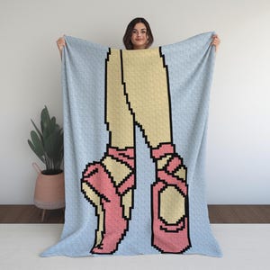 May include: A light blue blanket featuring a pixelated design of ballet dancer's legs and pink pointe shoes. The blanket has a repeating pattern of small, light blue shapes. The legs are beige with black outlines.