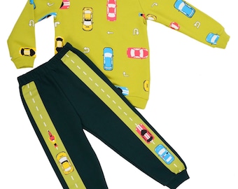 May include: A green and dark green two-piece children's clothing set with a long-sleeved shirt featuring a yellow, red, and blue car print and matching pants with a yellow stripe down the side.