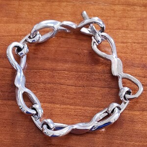 May include: A silver bracelet with a unique, twisted design. The bracelet has a clasp closure.