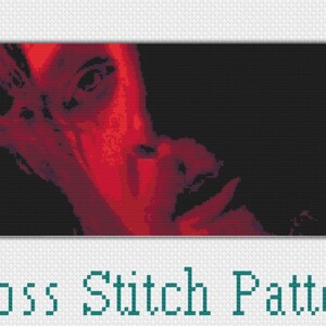May include: Cross stitch pattern of a person's face in red and black. The person's eye is visible and the face is partially obscured by a hand.