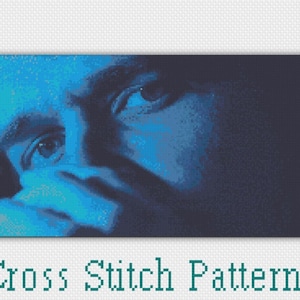 May include: A cross stitch pattern of a person's face in shades of blue. The person's eyes are visible, and they are looking to the side. The background is dark blue.