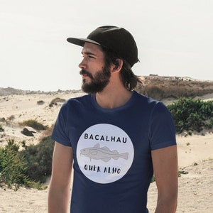 May include: A navy blue t-shirt with a white circle graphic featuring a cartoon fish and the text "BACALHAU QUER ALHO".