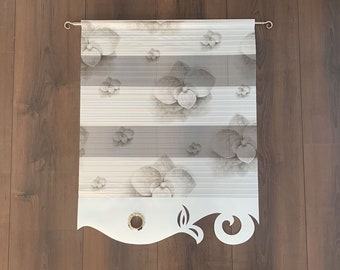 May include: A decorative window shade featuring a floral pattern of orchids in shades of gray and white. The shade has horizontal stripes and a decorative bottom edge with a cut-out design. The shade is suspended from a gold-colored rod.
