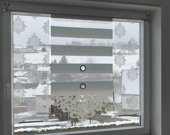 Könnte beinhalten: Ein Fenster mit weißem Rahmen zeigt eine mehrschichtige Jalousie. Die Jalousie hat abwechselnd horizontale Streifen in Hellgrün und Weiß, mit einem dekorativen Blumenmuster auf der linken Seite. Das Fenster blickt auf eine verschneite Landschaft.