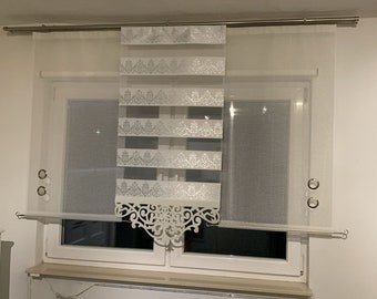 Könnte beinhalten: Mehrschichtige Fensterdekoration in Weiß und Silber. Das Design umfasst transparente und blickdichte Paneele mit dekorativen floralen Mustern. Der Vorhang wird an einer silbernen Stange aufgehängt und enthält Ösen zum Aufhängen.