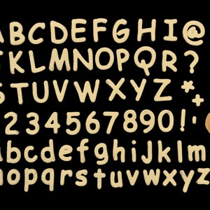 Op de afbeelding: Een set met hoofdletters en kleine letters, cijfers en symbolen gemaakt van een lichtbruin materiaal, mogelijk klei of deeg. De letters zijn alfabetisch gerangschikt en de cijfers numeriek. De symbolen omvatten een apenstaartje, een vraagteken, een sterretje en een uitroepteken.
