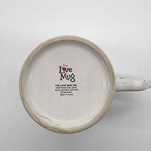 Puede incluir: Taza de cer&aacute;mica blanca con un coraz&oacute;n rojo y las palabras "The Love Mug" en negro. La taza tambi&eacute;n tiene el texto "THE LOVE MUG INC. WORTHINGTON, OHIO &copy;COLLECTIBLE EDITION MCMLXXXVI Made in Korea."